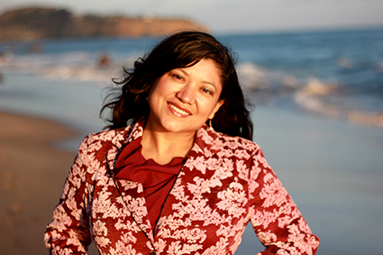 photograph of Reyna Grande smiling in a red blouse with the ocean behind her